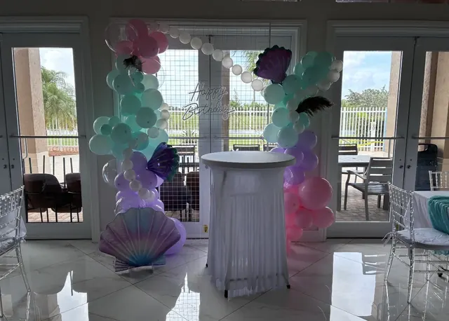 Mermaid balloon arch with pearls and a neon Happy Birthday sign on a grid wall